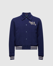 The Psycho Bunny KIDS DESERT COACH BOMBER JACKET (B0J428F200) in Evening Blue features white striped cuffs and hem, button-up front, and a small embroidered bunny logo on the left chest.
