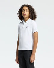 Against a plain, light-colored background, a person with curly hair wears a Psycho Bunny KIDS CLASSIC PIQUE POLO SHIRT - B0K001CRPC in white, crafted from soft Pima cotton and adorned with a small embroidered bunny logo on the chest.