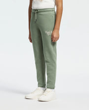 A person in Psycho Bunny's KIDS DESERT EMBROIDERED MODAL SWEATPANT (B0P489F200) with a wordmark on the upper left leg and white sneakers stands against a plain background. These green sweatpants feature soft stretch jersey fabric, an elastic waistband, and a drawstring for comfort.