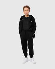 A young person in a black hoodie and Kids Levy Essential Fleece Sweatpants by Psycho Bunny, featuring a cartoon bunny design, stands smiling in white sneakers against a plain white background.
