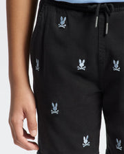 A person wears Psycho Bunny KIDS ALL OVER WILLIS STRETCH TENCEL SHORTS (B0R559F200) with a bunny and crossbones embroidery, elasticized drawstring waist. Only the lower torso and one hand are visible.