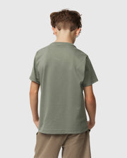 A young boy with short brown hair faces away, wearing a Psycho Bunny Kids Classic Crew Neck Tee in plain green and beige shorts. This 100% Pima cotton tee is ideal for back-to-school, set against a light grey background.