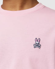Close-up of a person wearing Psycho Bunny's KIDS CLASSIC CREW NECK TEE - B0U014CRPC in light pink, made from 100% Pima cotton. It features an embroidered cartoon bunny head and crossbones logo near the chest—ideal for back-to-school outfits.