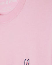Close-up of the KIDS CLASSIC CREW NECK TEE - B0U014CRPC from Psycho Bunny, a light pink shirt made from 100% Pima cotton. It features a small embroidered bunny ears and skull logo near the hem, ideal for stylish back-to-school outfits.