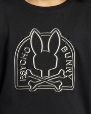 Close-up of the black KIDS MELBOURNE GRAPHIC TEE - B0U410F200 by Psycho Bunny, showcasing a logo with a stylized bunny head above crossed bones. Made from luxurious Peruvian Pima cotton, "Psycho Bunny" is elegantly written along the sides of the logo.
