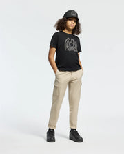 A person with curly hair is wearing a black cap, a Psycho Bunny KIDS MELBOURNE GRAPHIC TEE featuring line art, beige cargo pants, and black sneakers. They're standing casually against a plain white background with one hand in their pocket.