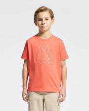 A young boy with light brown hair is wearing a Psycho Bunny KIDS MELBOURNE GRAPHIC TEE (B0U410F200) in orange, featuring a bunny and crossbones design. It's crafted from soft Pima cotton and paired with beige cargo pants against a plain white background.
