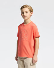 A boy in a colorful Psycho Bunny KIDS MELBOURNE GRAPHIC TEE (B0U410F200) with a bunny design stands against a white background. His left arm is bent slightly, and he's paired the shirt with comfy beige pants, creating a charming casual style.