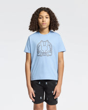 A person with curly hair wears an eco-friendly light blue KIDS MELBOURNE GRAPHIC TEE (B0U410F200) by Psycho Bunny, featuring a bunny and crossbones design. They're also in black shorts with small motifs against a plain light gray backdrop.