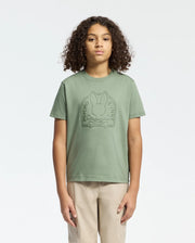 With curly hair and beige pants, a person faces forward wearing the KIDS MELBOURNE GRAPHIC TEE (B0U410F200) by Psycho Bunny, featuring a bold Bunny graphic on green Pima cotton, set against a plain white background.