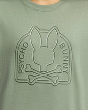 The KIDS MELBOURNE GRAPHIC TEE (B0U410F200) by Psycho Bunny features a soft Pima cotton Green shirt with a raised Bunny graphic in an arched frame, highlighting the bunny head above crossed bones and embossed "PSYCHO BUNNY," perfect for any wardrobe.