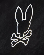 A black background with a white graphic design featuring the silhouette of a bunny's head, complete with large upright ears, positioned above two crossed bones. Perfect for customizing your waterproof bag or Psycho Bunny KIDS PARKER HYDROCHROMIC SWIM TRUNK - B0W646C200.