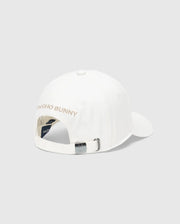The MENS NEW CASTLE EMBROIDERED GRAPHIC BASEBALL CAP by Psycho Bunny features a back view of an embroidered cotton twill design with "PSYCHO BUNNY" in light tan, embodying quiet luxury. It includes an adjustable strap with a metal buckle, a top button, and ventilation eyelets.
