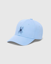 The Psycho Bunny Men's New Castle Embroidered Graphic Cap (B6A547F200) is a light blue cotton twill baseball cap. It features a small embroidered cartoon rabbit face with crossed bones, showcasing quiet luxury with a curved brim on a plain white background.