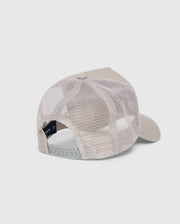 The MENS MALTON TRUCKER CAP - B6A797D200 by Psycho Bunny is displayed from behind, highlighting its adjustable snap closure. The beige cap boasts a 100% cotton solid front panel, mesh ventilation, and a curved brim against a plain light gray background.