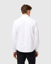 A person with short brown hair is standing with their back to the camera, wearing a Psycho Bunny Mens Arthur Jersey Shirt (B6C748D200) made from stretch Pima cotton, along with black pants. The background is a plain, light gray color.