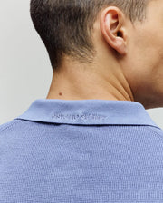 A close-up of the back of a man's neck and head, wearing Psycho Bunny's MENS LEETON JOHNNY COLLAR KNIT POLO (B6E562F200) in light blue, featuring "PSYCHO BUNNY" embroidered on the collar.