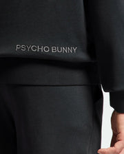 Close-up of someone in the Psycho Bunny MENS NEW CASTLE EMBROIDERED FRENCH TERRY HOODIE, with "Psycho Bunny" in white embroidery on the top's side; only part of the lower arm and upper body are visible, hinting at a style reflective of New Castle vibes.