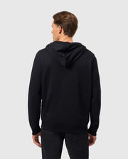 A person with short hair is wearing Psycho Bunny's Men's Levy Zip Fleece Hoodie (B6H720D200) and black pants, facing away from the camera. The background is plain gray.
