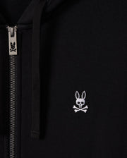 Close-up of the Psycho Bunny MENS LEVY ZIP FLEECE HOODIE - B6H720D200 in black, featuring a silver zipper on the left side. This cotton zip hoodie displays a small white logo of a rabbit skull and crossbones on the right side.