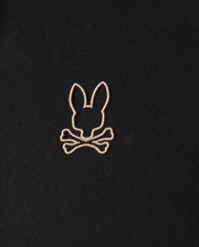 The Psycho Bunny MENS JAMES PREMIUM HOODIE - B6H789D200 features a black premium jersey fabric adorned with an embroidered design of a bunny head above two crossed bones in white stitching.