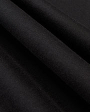 Close-up of black fabric folds with a textured surface. The material of the MENS JAMES PREMIUM HOODIE - B6H789D200 by Psycho Bunny, reminiscent of essential fleece, appears soft and smooth, showcasing a rich and deep black color. The folds create gentle shadows and highlights, enhancing the fabric's texture.