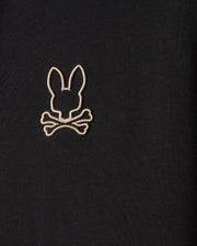 Psycho Bunny's MENS JAMES PREMIUM ZIP HOODIE - B6H793D200 features black fabric adorned with an embroidered rabbit head with ears pointed up, positioned above two crossed bones. The design is outlined in white thread, making this zip-up hoodie the epitome of stylish warmth, crafted from a premium jersey.
