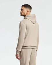 A man dressed in a Psycho Bunny MENS LEVY ESSENTIAL FLEECE HOODIE - B6H859D200 and coordinated sweatpants, both made from 100% cotton, stands sideways gazing to the left against a plain white backdrop.