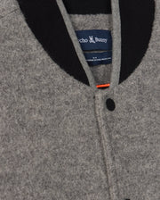 Close-up of a Men's Tom Wool Bomber Jacket (B6J744D200) by Psycho Bunny, featuring a gray wool body with a black collar and single black button. The inside label reads “Psycho Bunny” with a small chenille Bunny patch above it. The seam of the button placket and the top of the collar are visible, highlighting the fine craftsmanship using virgin wool.