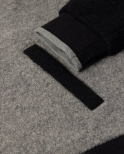 Close-up of the Psycho Bunny Men's Tom Wool Bomber Jacket (B6J744D200) in grey and black, featuring a sleeve cuff with both grey and black sections, and a strip of black Velcro. The textured grey fabric complements the partially attached Velcro strip on this premium wool bomber.