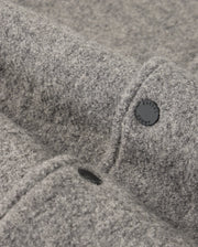 Close-up of a gray fabric texture showcasing the soft, felt-like material of the MENS TOM WOOL BOMBER JACKET - B6J744D200 by Psycho Bunny. Two black buttons are visible, partially embedded in the premium wool jacket, with one clearly displaying an engraved word in uppercase letters. The surface appears smooth and cozy.