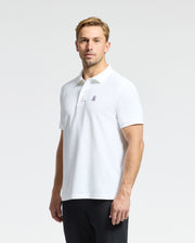 Dressed in the MENS CLASSIC PIQUE POLO SHIRT - B6K001ARPC by Psycho Bunny, featuring a small logo on the chest, a person stands against a plain background. Their white Pima cotton shirt is stylishly paired with dark pants for an effortlessly chic appearance.
