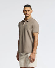 A man stands against a plain background, wearing a Psycho Bunny MENS CLASSIC PIQUE POLO SHIRT - B6K001CRPC with a small chest logo and light beige shorts. He faces forward with a neutral expression.