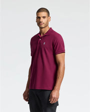 A man in a maroon Psycho Bunny MENS CLASSIC PIQUE POLO SHIRT (B6K001Z1PC) made from Pima cotton stands against a plain backdrop. The shirt has a small embroidered Bunny logo on the chest. He has short hair and faces the camera.