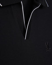 Close-up of a black Pima cotton MENS EAST HILLS JOHNNY COLLAR POLO SHIRT - B6K331B200 by Psycho Bunny with contrasting white piping along the Johnny collar. The shirt features an embroidered logo of a rabbit with crossbones on the left chest. The fabric texture is evident, giving it a premium, solid pattern look.