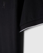 Close-up of a Psycho Bunny MENS EAST HILLS JOHNNY COLLAR POLO SHIRT - B6K331B200 sleeve with a subtle embroidered logo on the chest. The sleeve boasts a clean, minimalistic design featuring a single white stripe along the edge. Its solid pattern and neutral background enhance its timeless appeal.