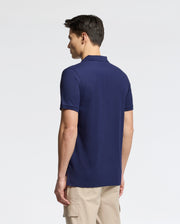 A man in a Psycho Bunny MENS NICHOLSON RIB COLLAR PIQUE POLO, navy blue with an embroidered logo, and beige cargo shorts stands against a plain white background.