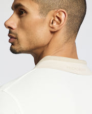 A man with short hair and light facial hair wears the Psycho Bunny MENS NEW CASTLE PIQUE POLO (B6K487F200), turned to show the back collar where “PSYCHO BUNNY” is subtly embossed on the soft Pima cotton.