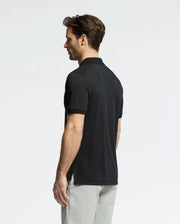 A man with brown hair, facing away, wears a Psycho Bunny MENS TREVOR PERFORMANCE PIQUE ZIP UP POLO in black and light gray pants against a plain light background.