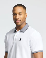 A man with short hair and a trimmed beard wears the Psycho Bunny MENS JONAS STRIPE COLLAR PIQUE POLO (B6K583F200) featuring a gray collar, micro-stripe details, and a black bunny logo, against a plain light background.