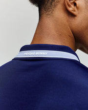 Close-up of the back of a person’s neck and shoulders wearing the Psycho Bunny MENS FORREST SPORT PIQUE POLO in navy blue, with a light blue and white striped collar, "PSYCHO BUNNY" embroidery, and breathable, moisture-wicking fabric.
