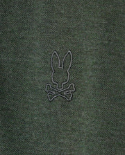 A close-up of the dark green fabric on the Psycho Bunny MENS JAMES PREMIUM PIQUE POLO SHIRT - B6K945D200, showcasing an embroidered black outline of a rabbit head with long ears, positioned above a pair of crossed bones.