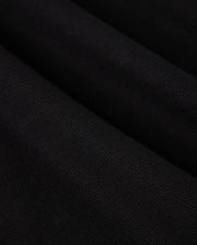 Close-up view of a black Pima cotton MENS MALTON PIQUE POLO SHIRT - B6K950D200, showcasing its texture and weave pattern. The material is slightly folded, creating diagonal lines and subtle highlights. The Psycho Bunny surface appears smooth and uniform, accentuating the exquisite detail.
