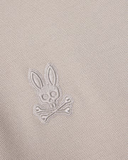 Close-up of the MENS MALTON PIQUE POLO SHIRT - B6K950D200 fabric in a diamond pique pattern, featuring an embroidered skull and crossbones design with rabbit ears, encapsulating the playful Psycho Bunny style. The thread color matches the fabric, creating a subtle and integrated appearance.