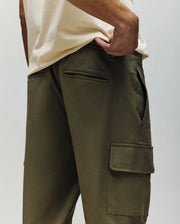 A person models the Psycho Bunny MENS LLOYD CARGO JOGGER - B6P159B200 in olive green, paired with a cream shirt, highlighting the jogger’s side and back pockets, relaxed fit, and detachable keychain on a belt loop.