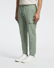 A person is wearing Psycho Bunny's MENS LLOYD CARGO JOGGER - B6P159B200 in light green, with a drawstring waist and large side pockets, paired with white sneakers. They're standing against a plain white background.