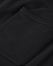 Close-up of the Psycho Bunny MENS LEVY ESSENTIAL FLEECE SWEATPANT - B6P721D200 in black, featuring a small, neatly sewn pocket. The texture appears soft and smooth, resembling premium fleecy cotton sweatpants, with the pocket positioned slightly off-center to highlight the clean stitching around its edges. The fabric drapes naturally, revealing subtle folds.