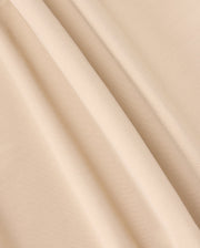 A close-up photograph of beige-colored fabric with a soft, smooth texture. The fabric, similar to that of the Psycho Bunny Mens Maverick 10K Pant (B6P788D200), is draped in gentle folds, creating light and shadow variations across its surface.