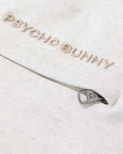 Close-up of the MENS JAMES PREMIUM SWEATPANT in a light-colored cotton-blend, featuring "Psycho Bunny" embroidered above a zipped pocket. The zipper pull is adorned with a subtle bunny logo, enhancing the comfort of this sleek design by Psycho Bunny.