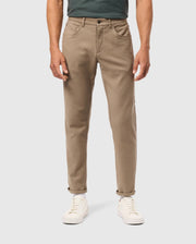 A person stands confidently in Psycho Bunny's MENS HAYS TWILL PANT - B6P894D200, expertly crafted from a cotton-blend twill for unbeatable comfort. The khaki pants feature rolled cuffs and are paired with white sneakers, while a hint of green shirt peeks through. The minimalist white background emphasizes the ensemble’s effortless style.